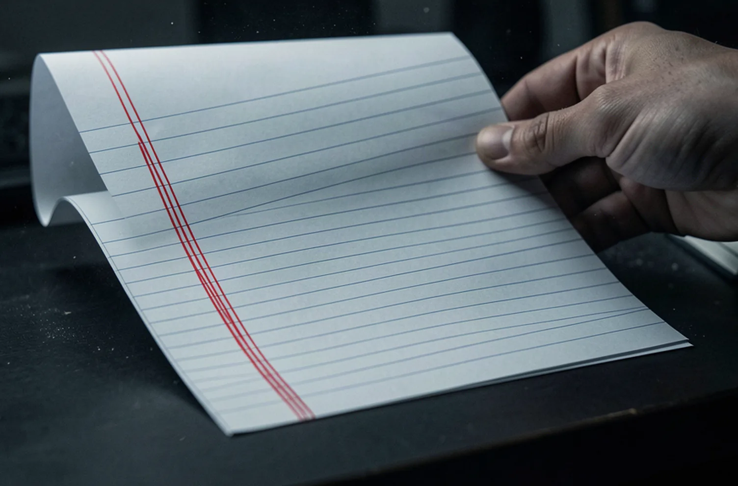 A printed ruled sheet held in one hand with several rows marked with heavy red pen strokes