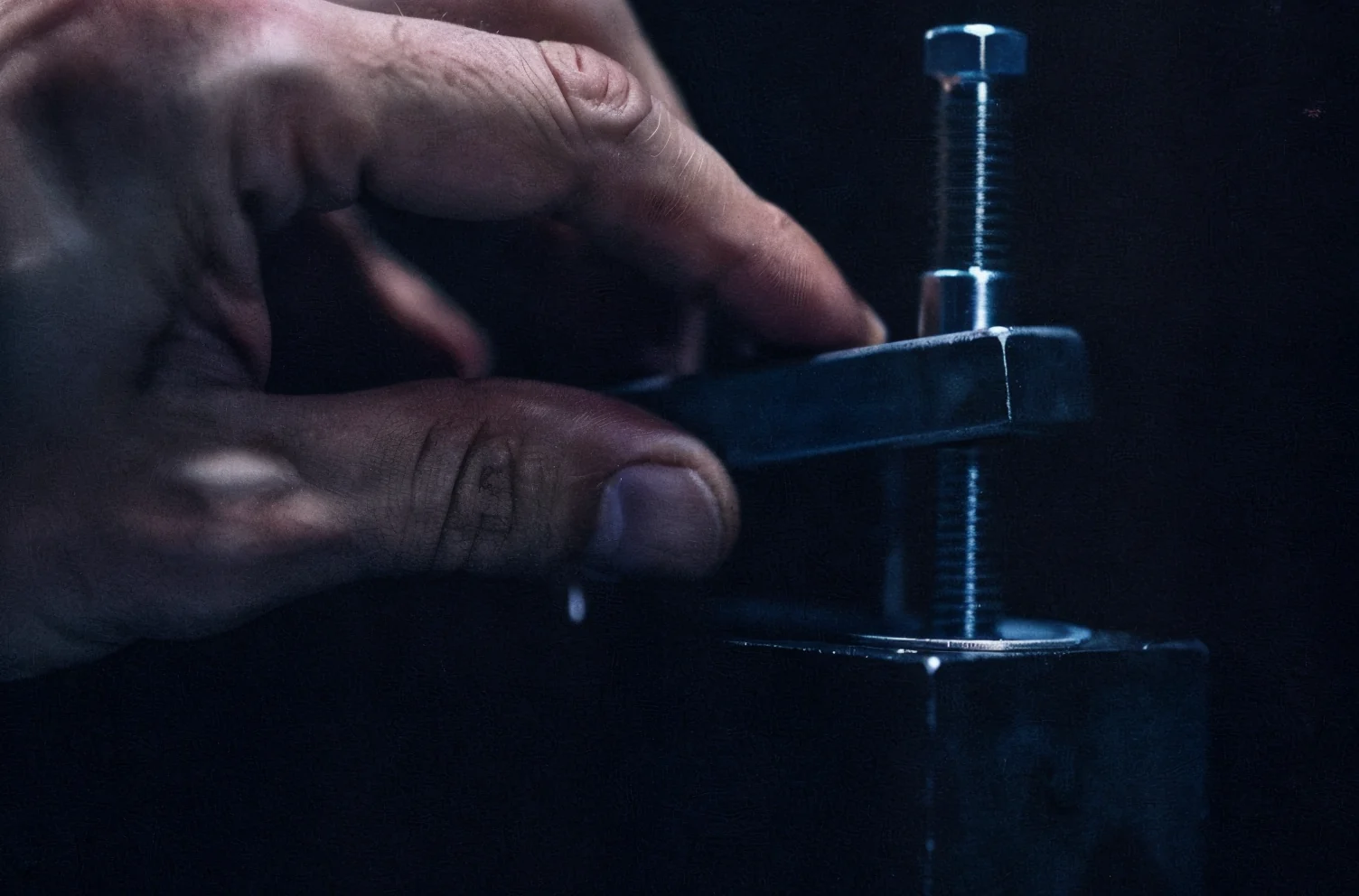 A hand forcing an oversized precision bolt toward a hole that is plainly too small in a small dark housing.